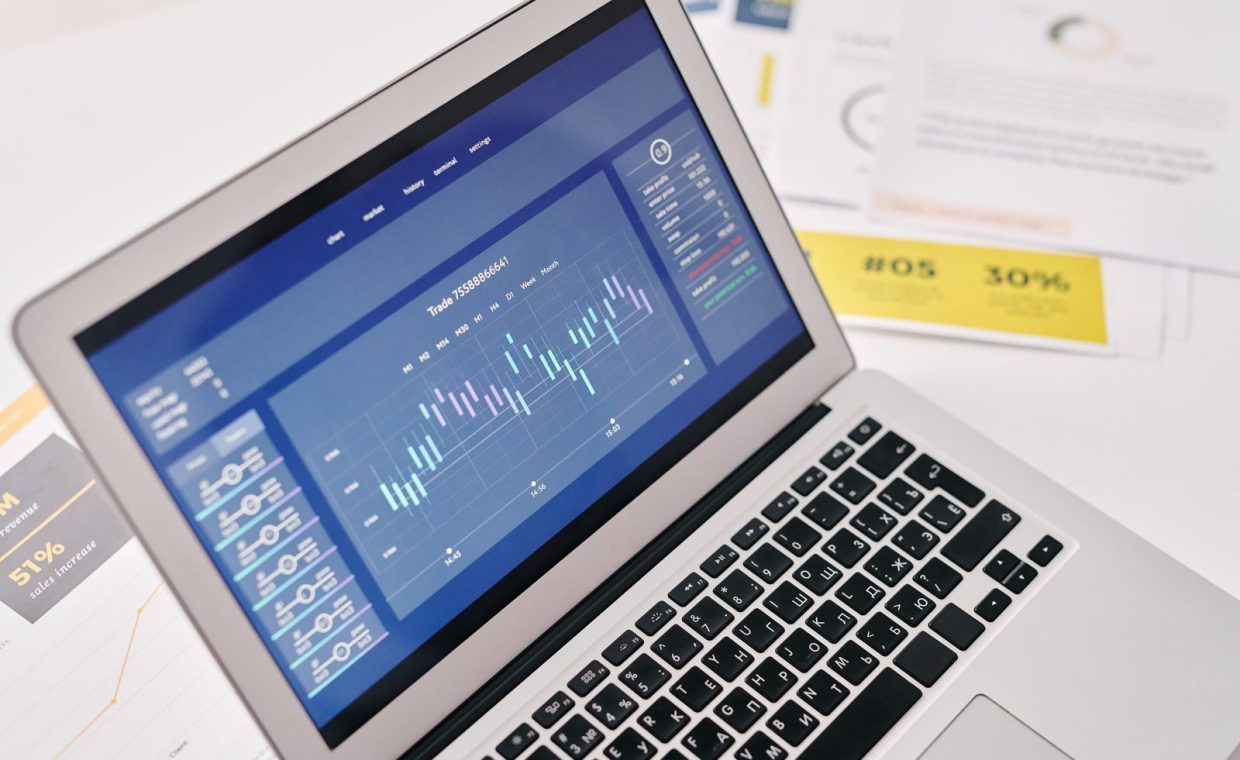 Open laptop displaying financial graphs and analytics with documents nearby, ideal for business presentations.