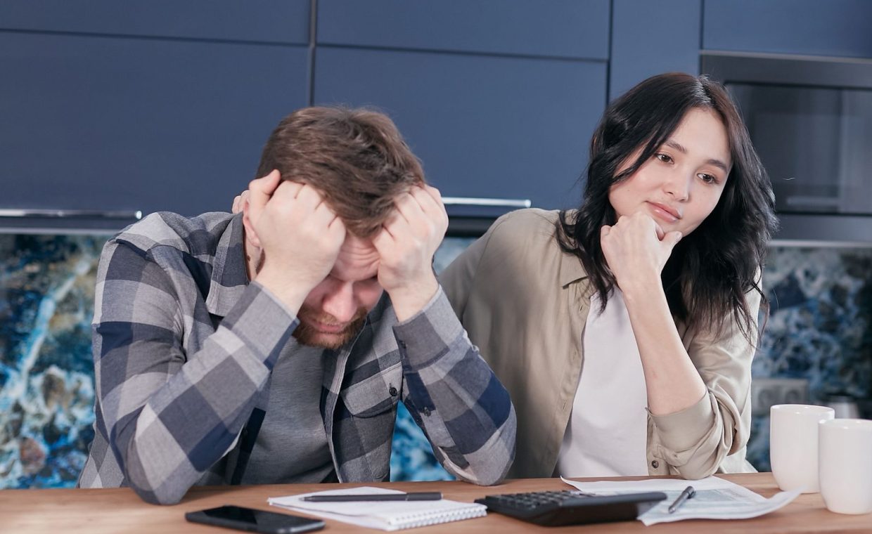 A couple looking worried while reviewing financial documents at a kitchen table.