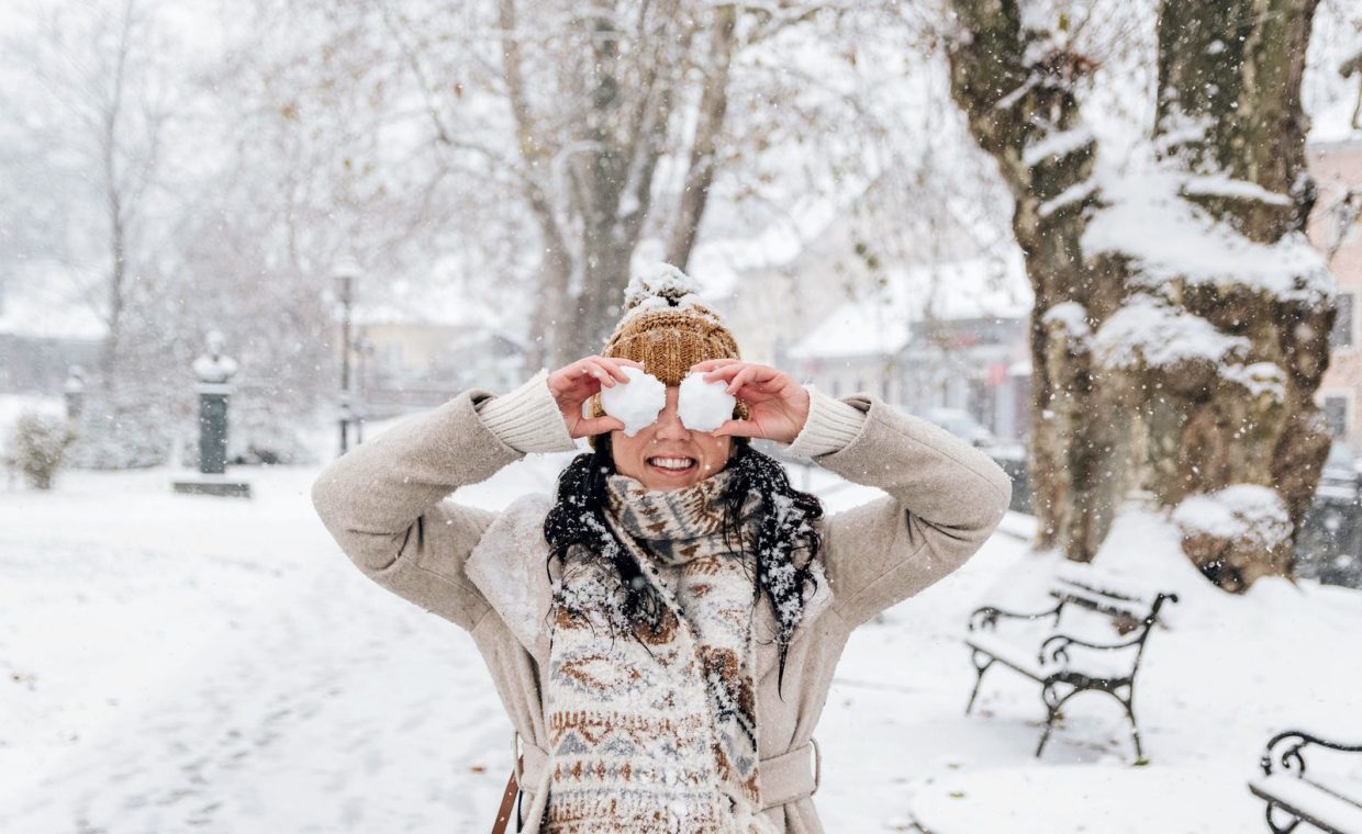 Woman enjoying a snowy winter day by playfully holding snowballs in a park.