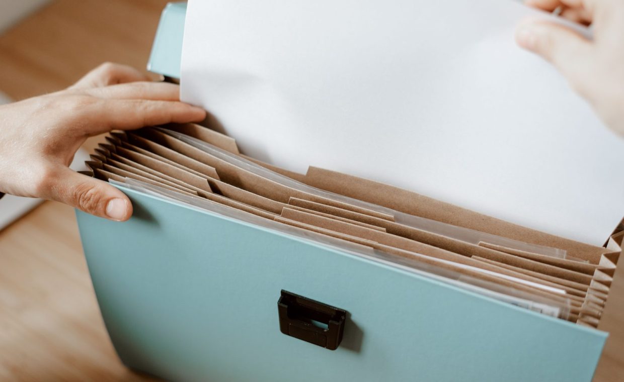 Crop faceless person putting sheet of paper in briefcase for documents placed on table