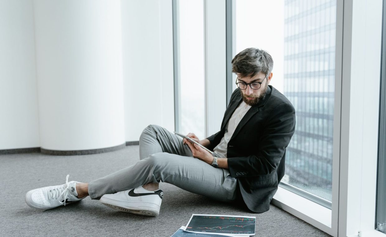 A man in an office setting using a tablet to analyze stock market data with graphs.