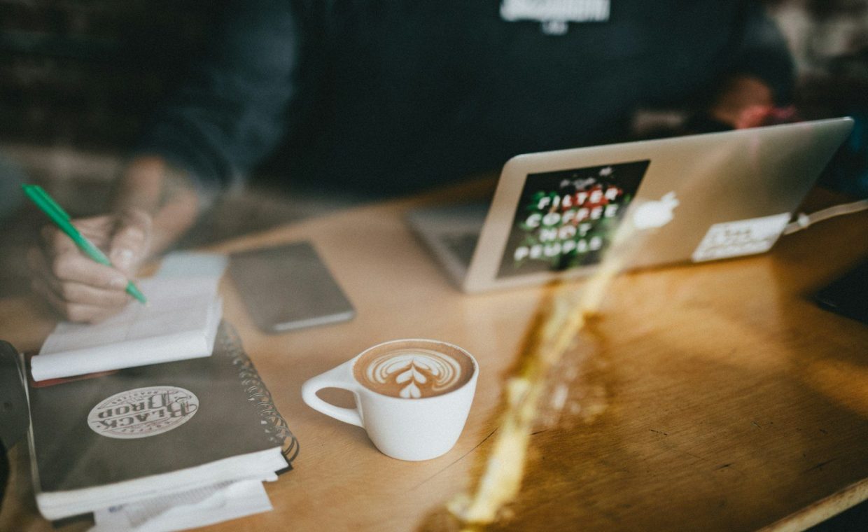 cappuccino art on white ceramic mug beside MacBook Air