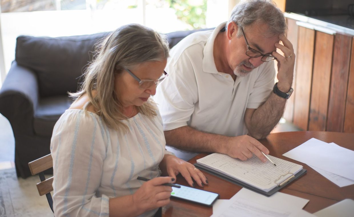 Elderly couple reviewing bills and documents at home, focusing on finances and technology.