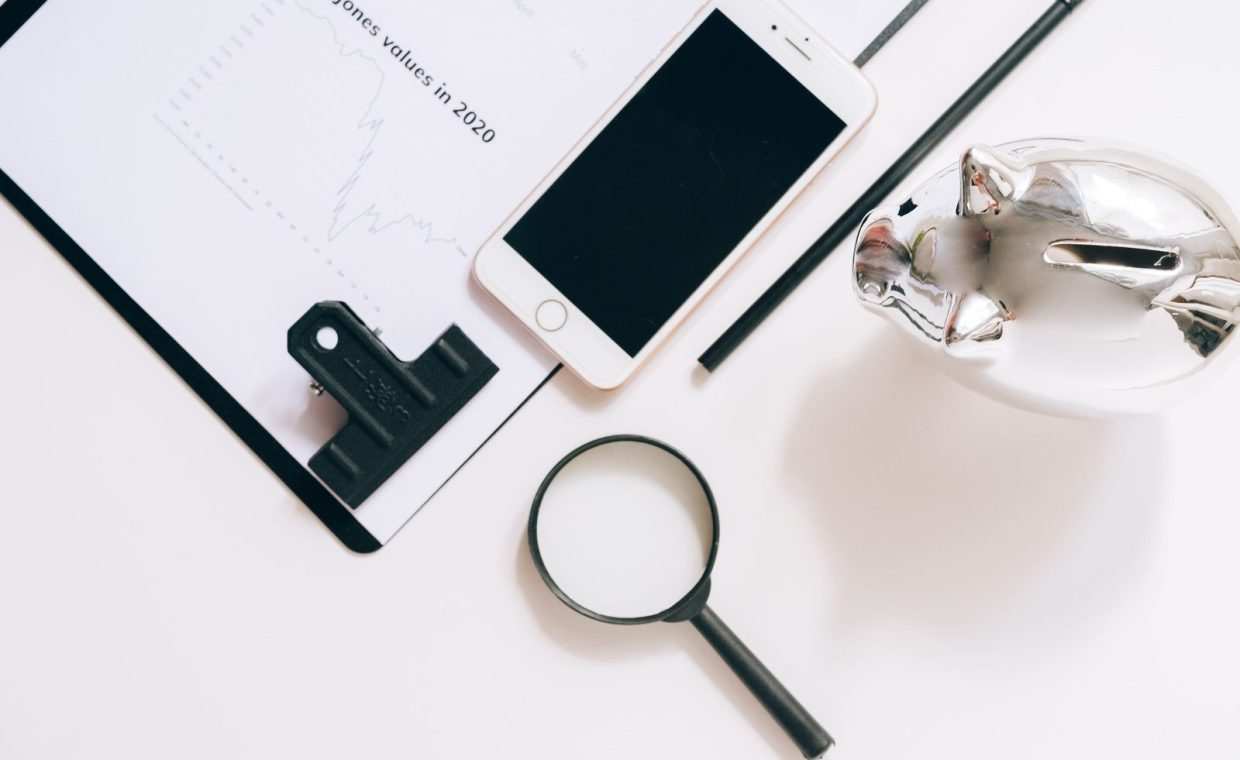 A flat lay of financial documents with a smartphone, magnifying glass, and piggy bank.