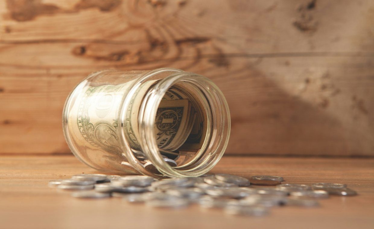 Glass jar with money and coins spilled on table