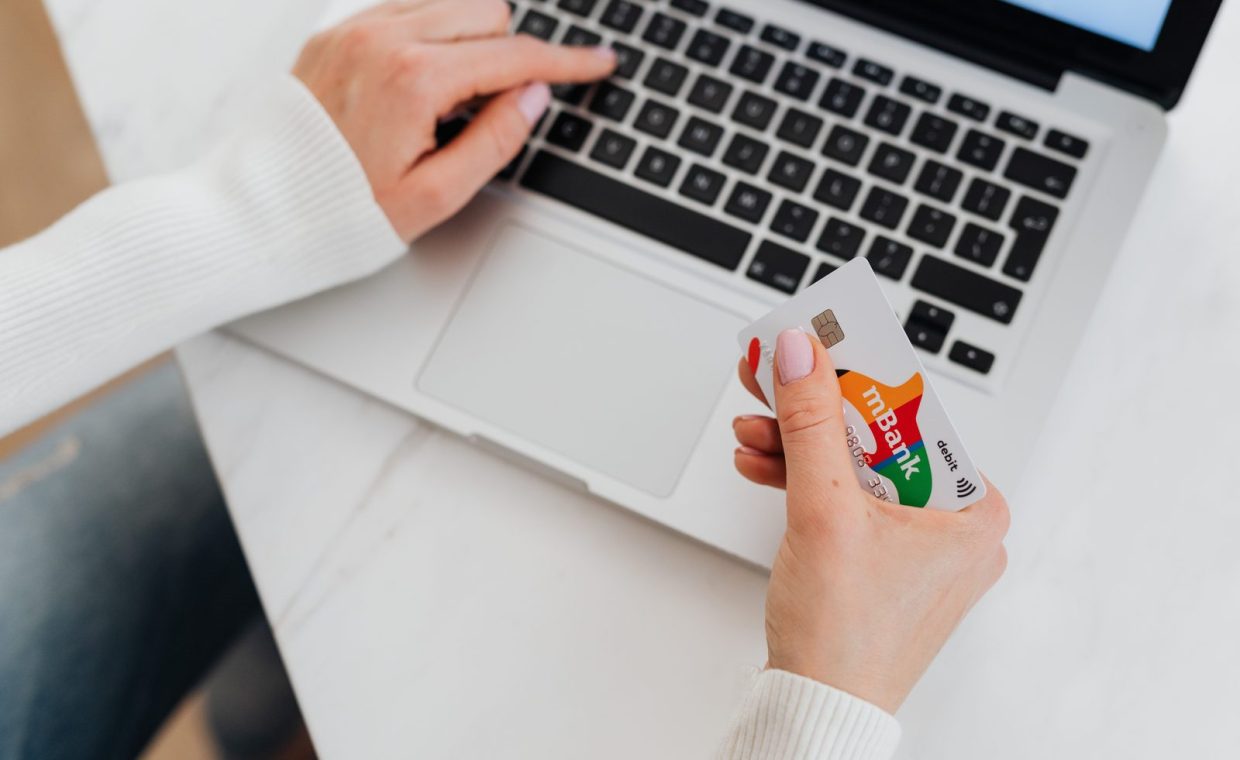 Close-up of a person using a laptop and holding a credit card for online shopping.
