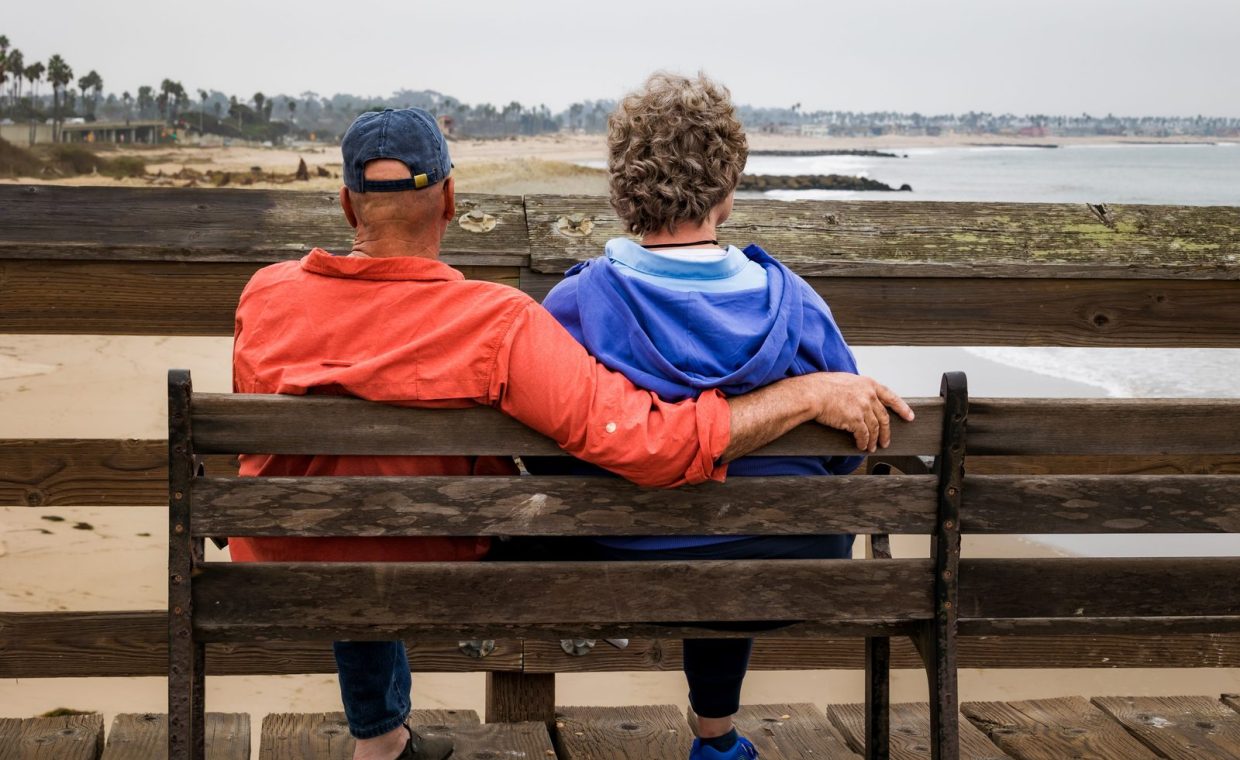 Senior couple enjoying a peaceful moment on a wooden bench overlooking the calm beach.