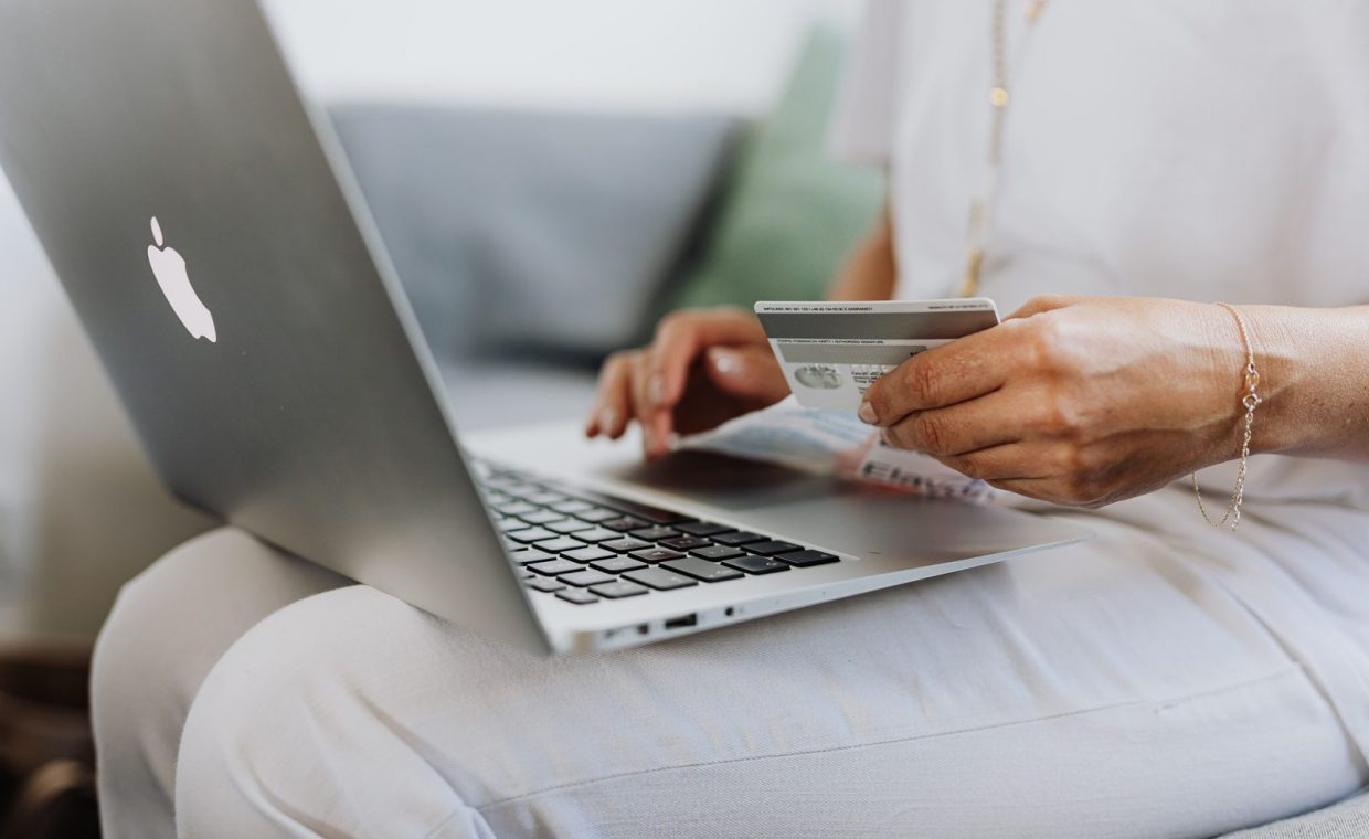 Close-up of a person holding a credit card while shopping online using a laptop at home.