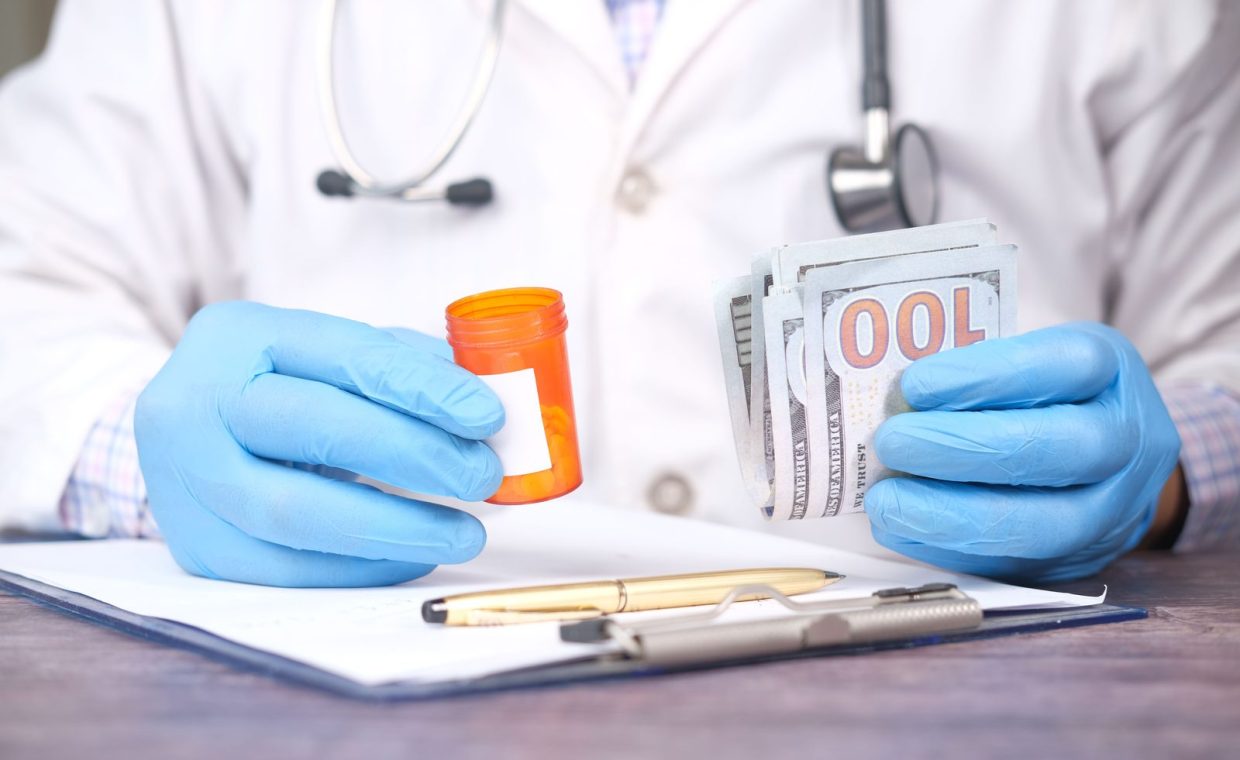 Doctor in gloves holding pill bottle and cash, highlighting medical expenses.