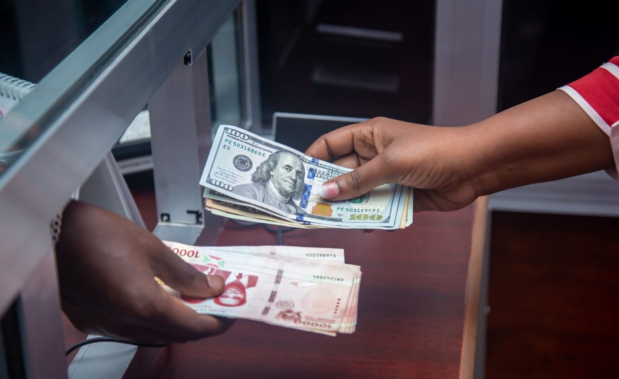 Hands exchanging US and local currency at a bank counter, signifying international finance.