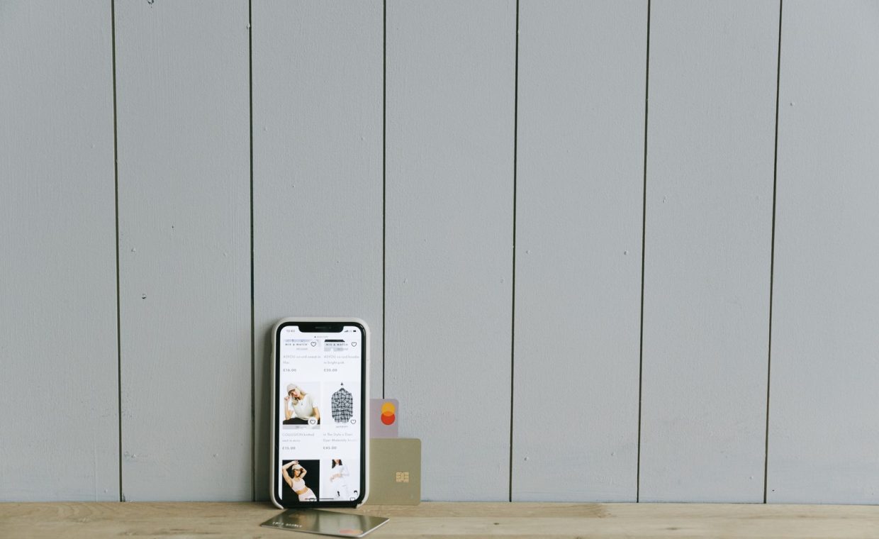 A smartphone displaying an ecommerce site with a credit card, set on a wooden surface, depicting online shopping.