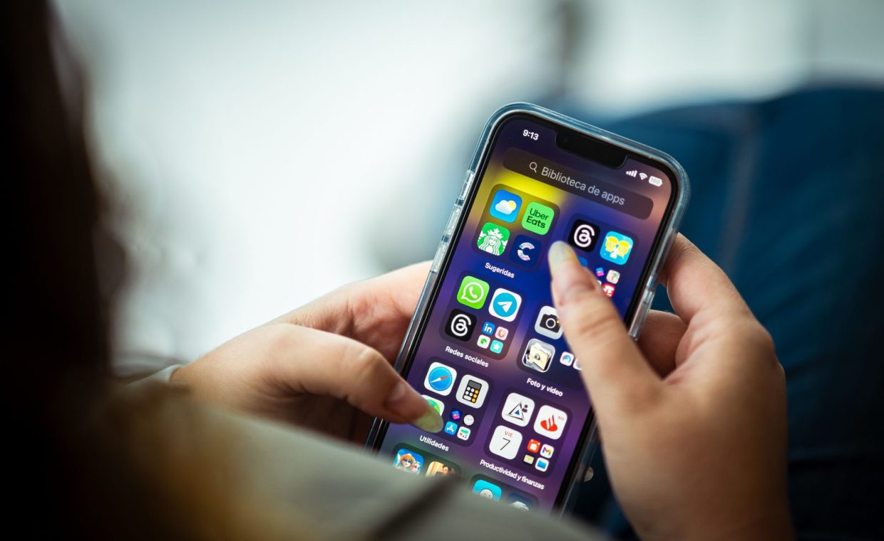 Close-up of a woman holding a smartphone displaying various apps.