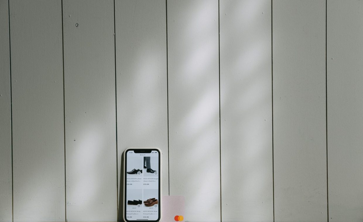 A smartphone and credit card sit on a wooden surface with soft lighting shadows.
