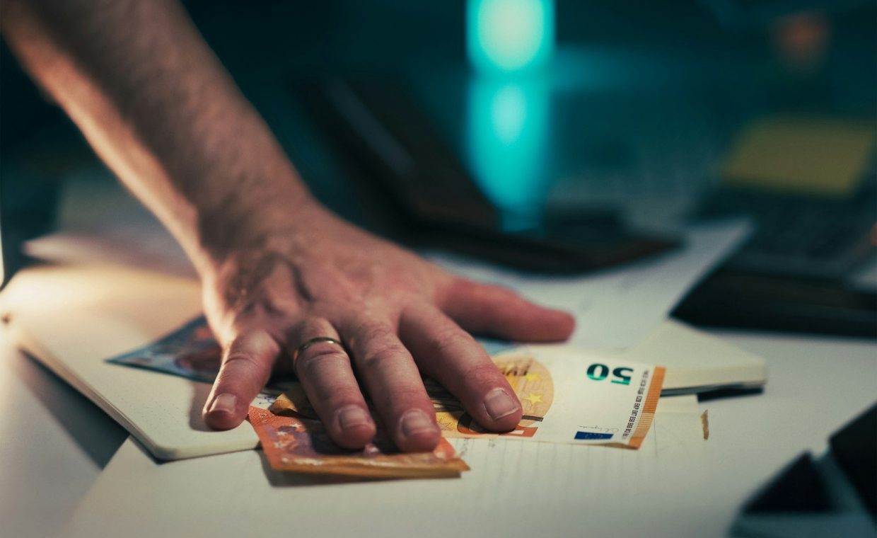 Hand reaching for euro banknotes on a table.