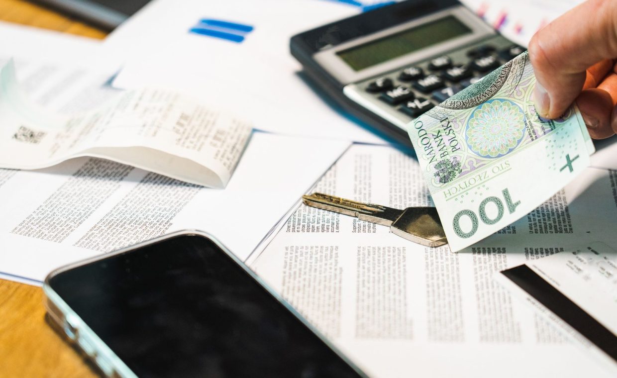 Close-up of financial documents, calculator, and Polish Zloty currency on a desk.