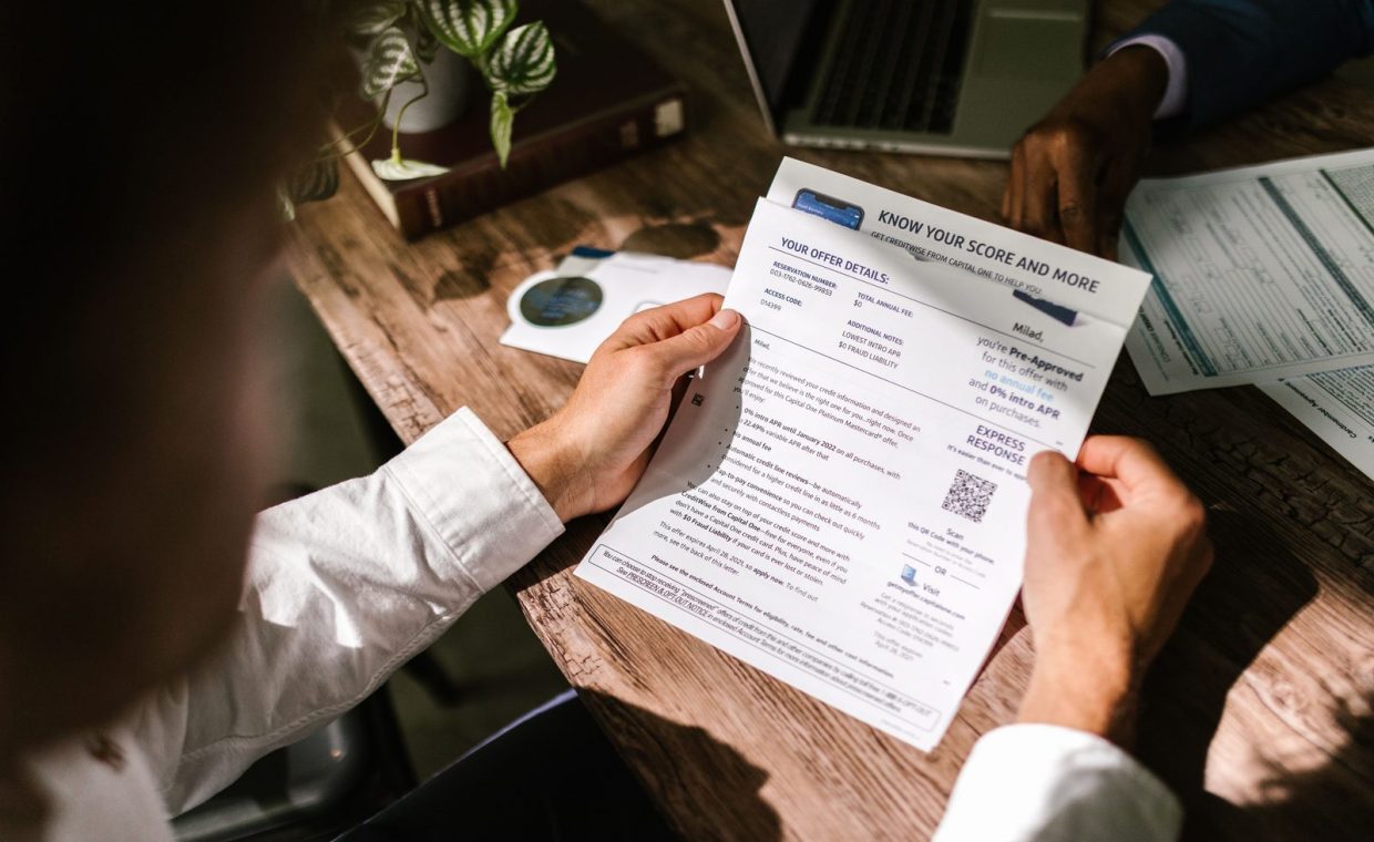 An adult man examining a financial document under natural light at a wooden desk, emphasizing finance and reading.