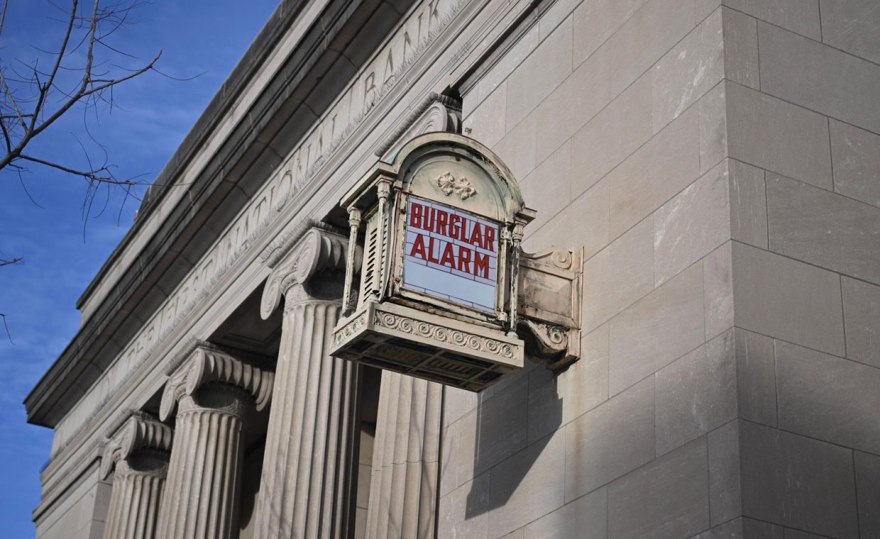 A historical neoclassical building with a prominent burglar alarm sign.