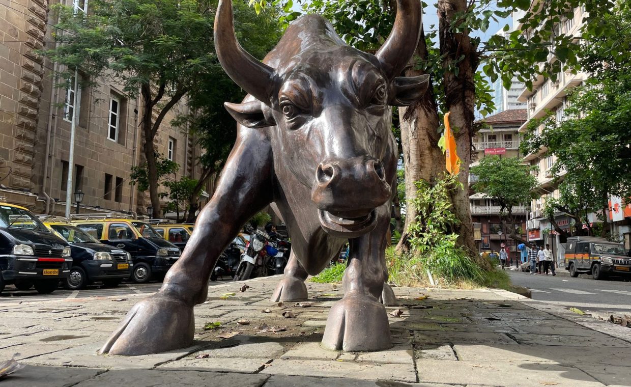 A prominent bull statue amidst a bustling urban street scene showcasing art and architecture.